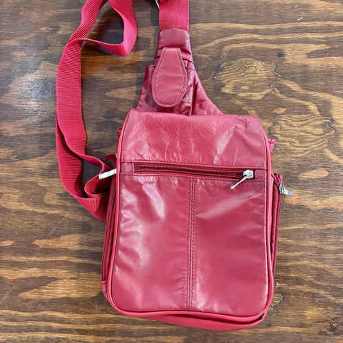 Red leather sling bag on a wooden surface