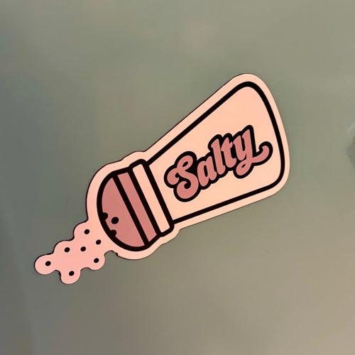 Magnet of a saltshaker labeled 'Salty' on a green surface.