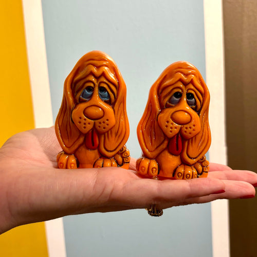 Two small dog salt and pepper figurines held in a hand against a colorful background