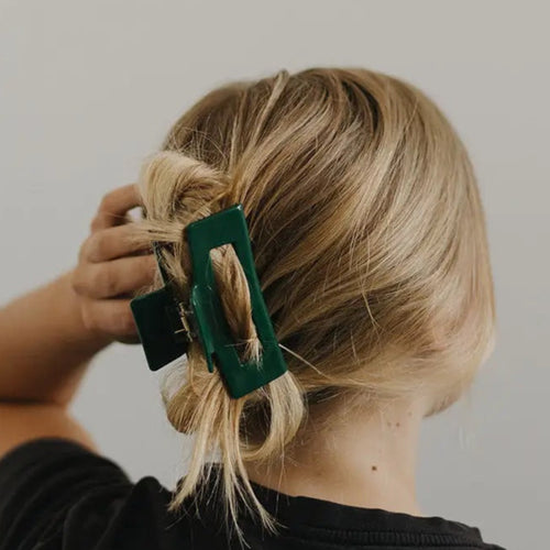 Person with blonde hair tied back using a green hair clip against a plain background