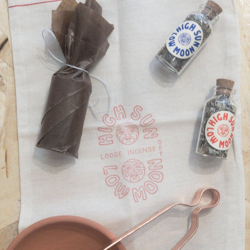 wrapped charcoal, two bottles of loose insence balled high sun low moon, a clay dish and copper tongs laid upon a burlap bag labelled High Sun Low Moon Loose Incense Set